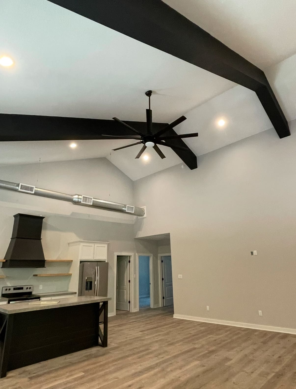 Modern kitchen with vaulted ceiling and exposed black beams reflects true Barndo style, featuring a large black ceiling fan, stainless steel appliances, and light wood flooring—perfect inspiration for any home builder.