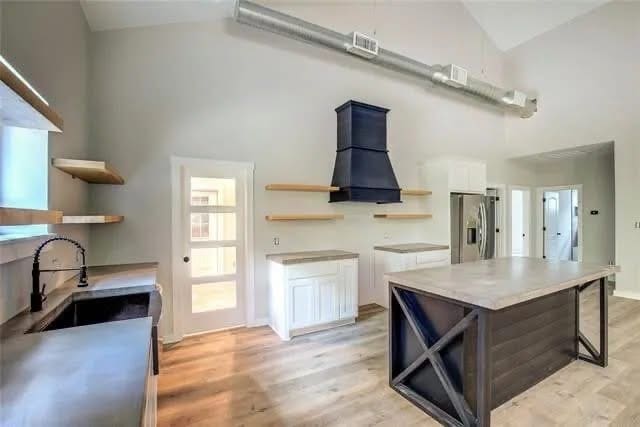 Modern kitchen by a custom home builder features light wood floors, open shelving, a large island, stainless steel appliances, and a black range hood under exposed ductwork—perfect for your dream barndo or unique living space.