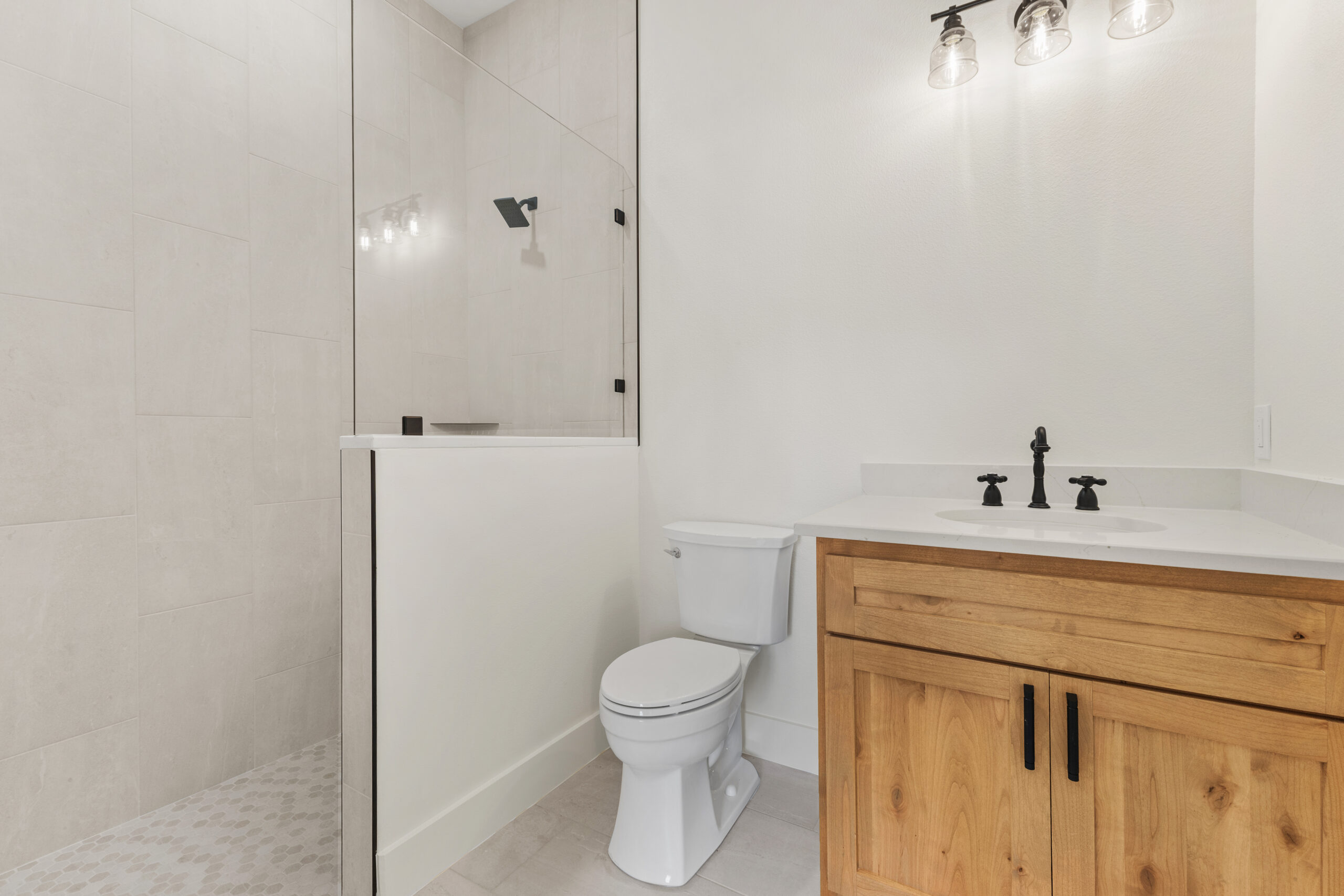 Modern bathroom with a glass-enclosed shower, white fixtures, and a wooden vanity featuring black hardware.