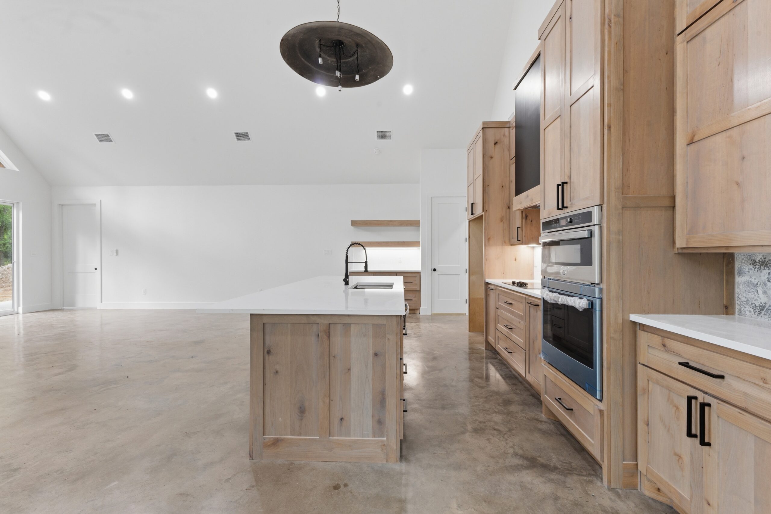 Bright open kitchen with a large wooden island, natural wood cabinets, and stainless steel double ovens along the right wall.