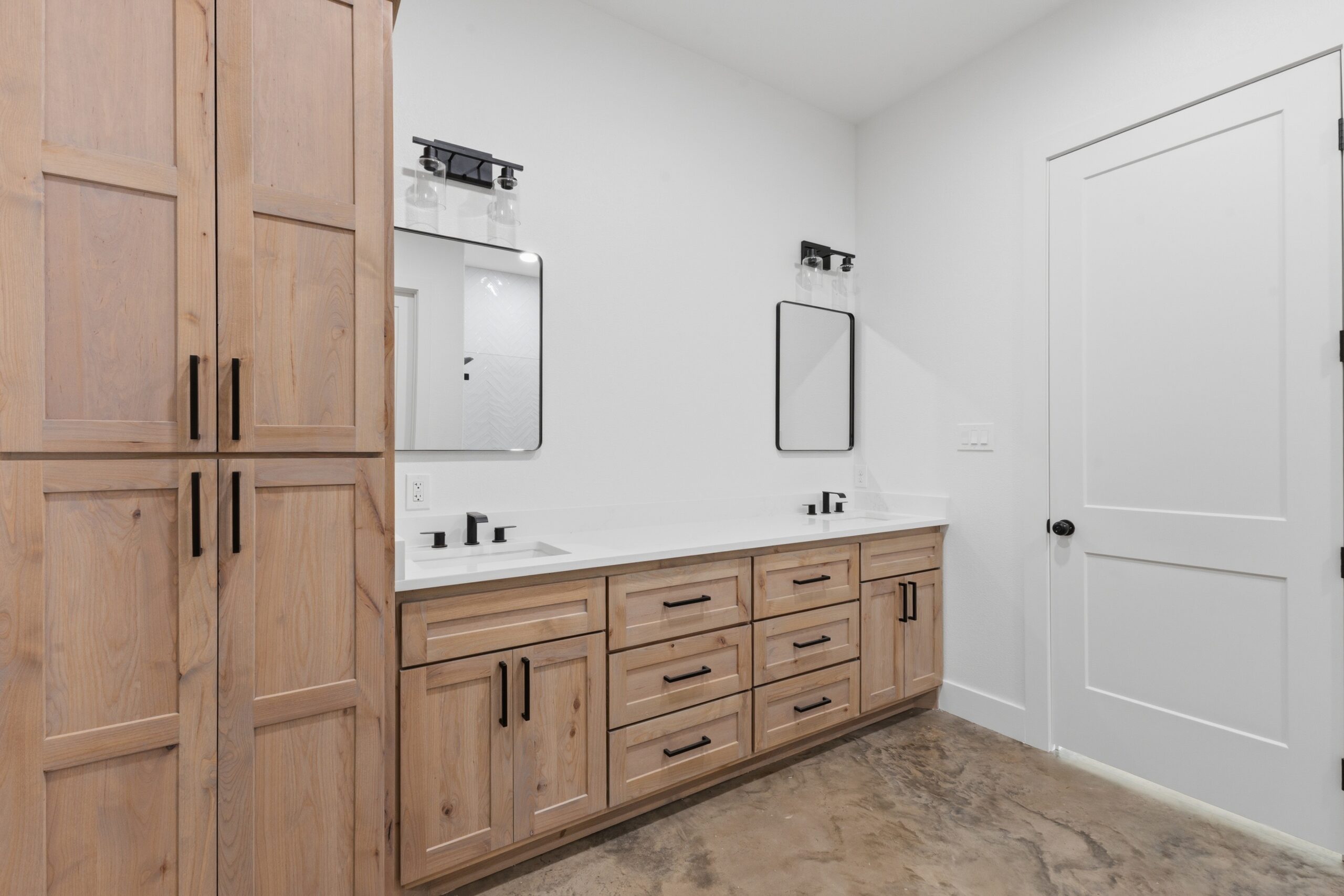 Wooden bathroom vanity with multiple drawers and two sinks, against white walls and mirrors above.