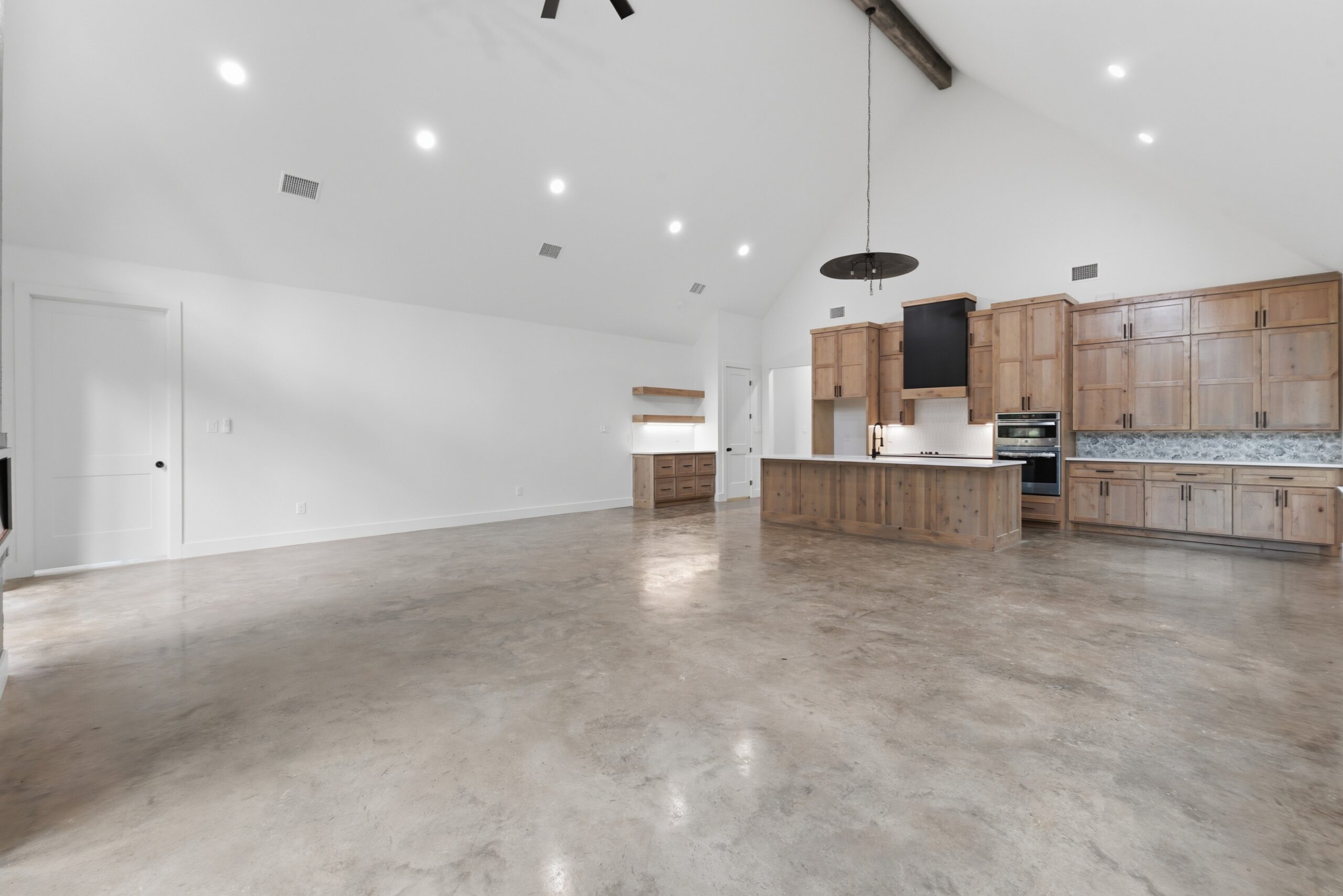 Spacious modern kitchen with wooden cabinets, large island, stainless steel appliances, high ceiling, and polished concrete floors in an open-plan layout.