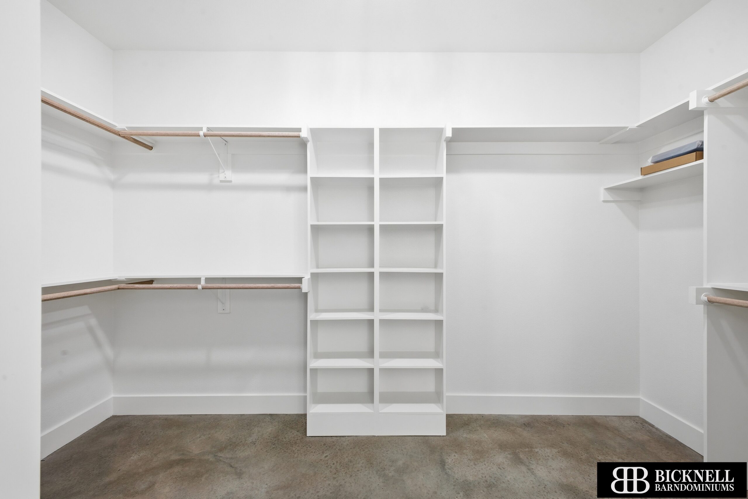 Empty white walk-in closet featuring a central cubby shelving unit and wooden clothing rods along both sides.