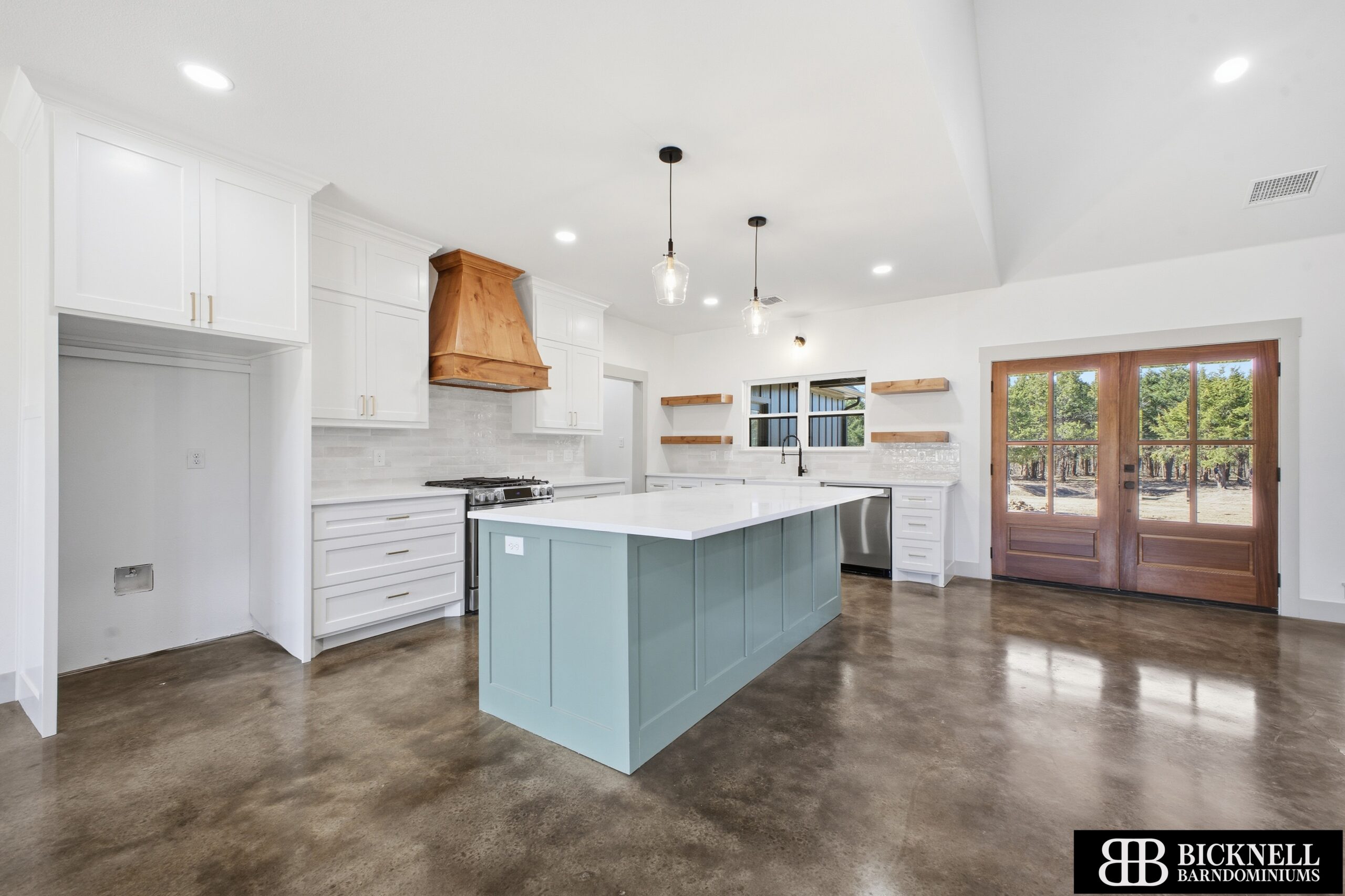 Bright modern kitchen with white cabinets, a blue island, and a wooden range hood under pendant lights.