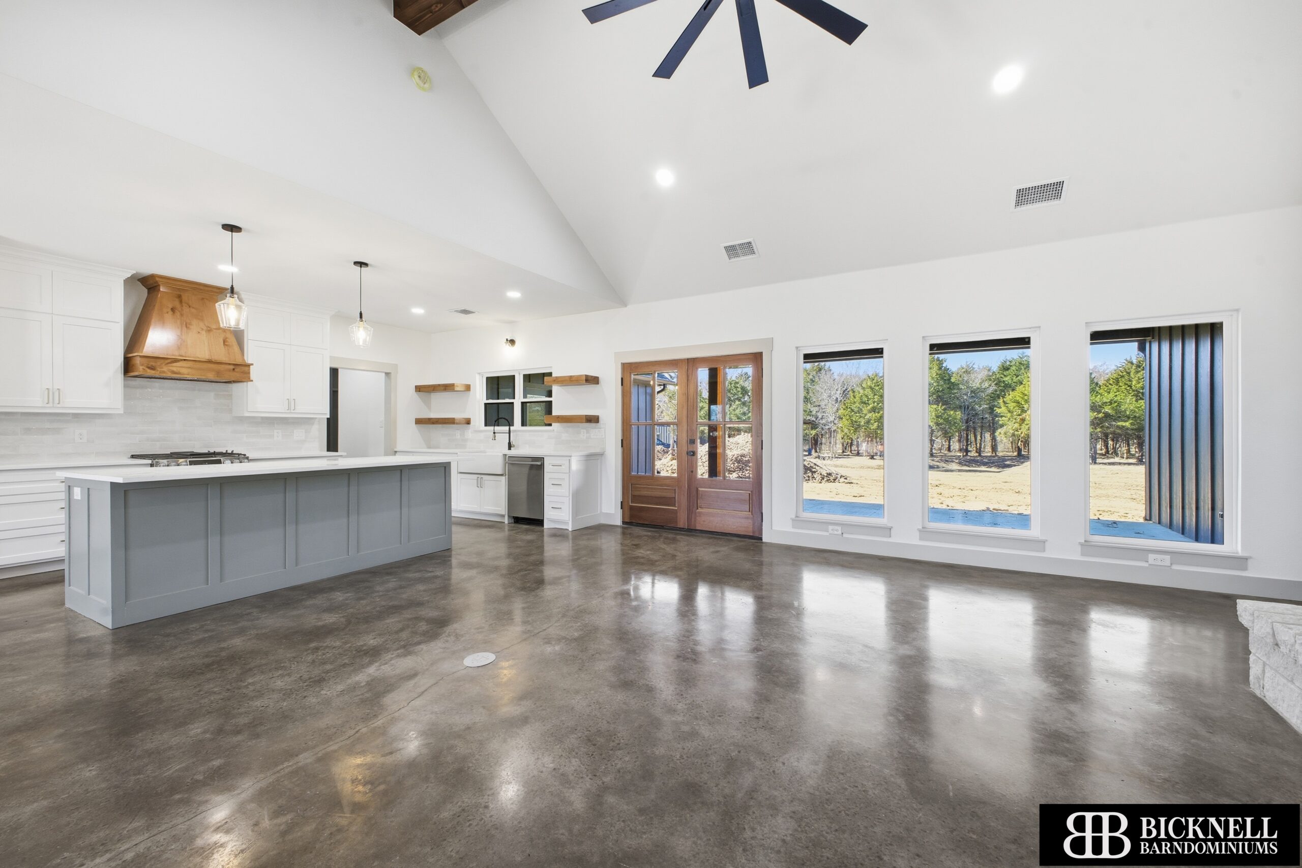 Spacious modern kitchen and living area with polished concrete floors, large windows, white walls, an island, and wooden accents.