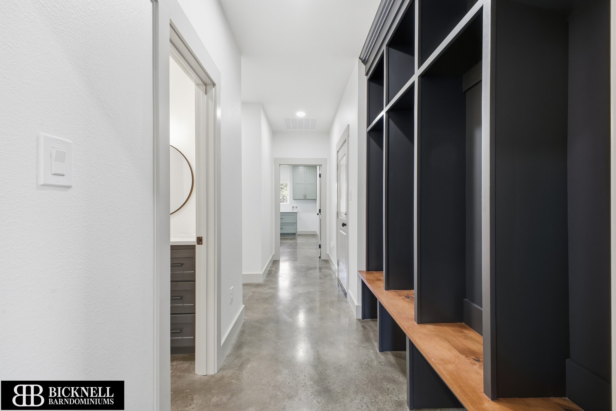A hallway with polished concrete floors, dark built-in shelves with a wooden bench, and doorways leading to other rooms in a modern home.