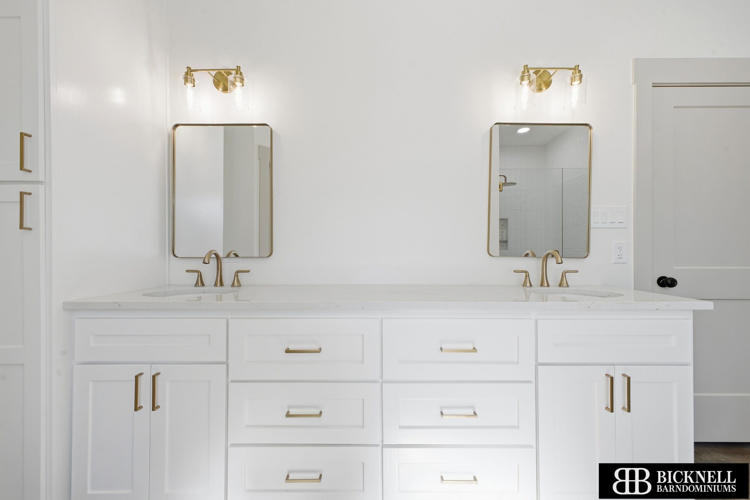 A modern white double-sink bathroom vanity with gold hardware, two mirrors, and wall-mounted light fixtures above each sink.